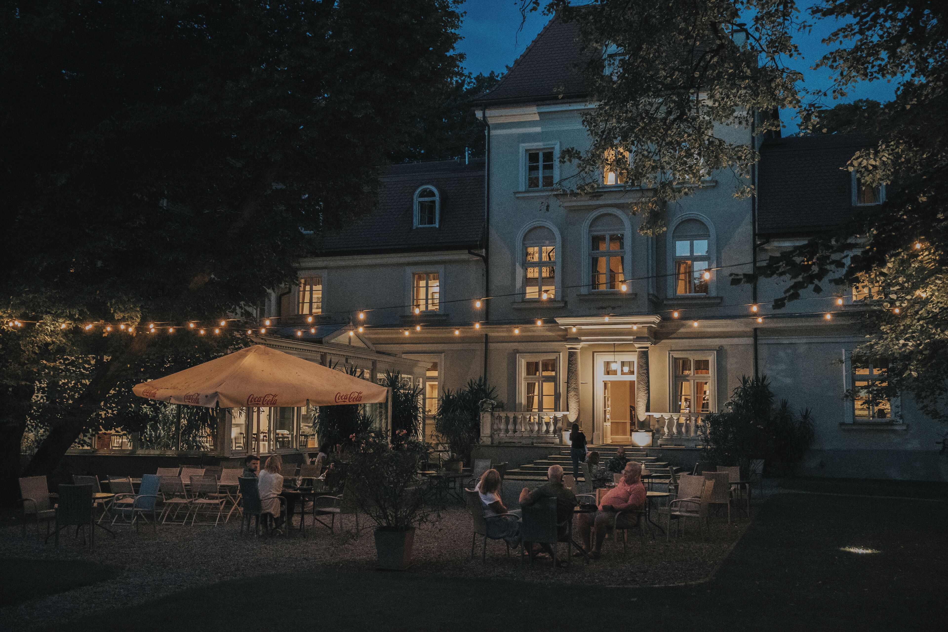 A large building with a patio area featuring outdoor seating and string lights. - Dwór Sieraków (Dobczyce)