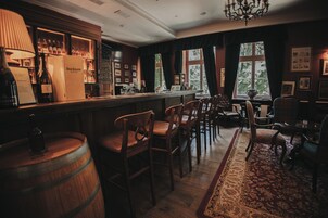 Uma área de bar com mobiliário de madeira, um candelabro e vista para o exterior através de amplas janelas.