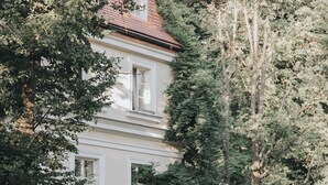 A building with a red roof, white walls, and multiple windows. There are trees and potted plants around the building. - Dwór Sieraków (Dobczyce)