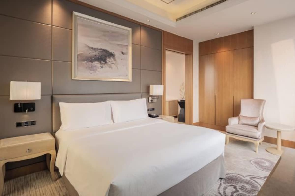 Habitación de hotel moderna con una cama grande, lámparas de noche, una silla y un cuadro abstracto de grandes dimensiones en la pared.
