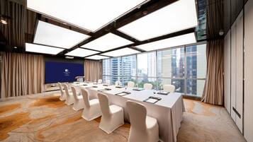 A conference room with a long table, white chairs, and a large window with a city view.
