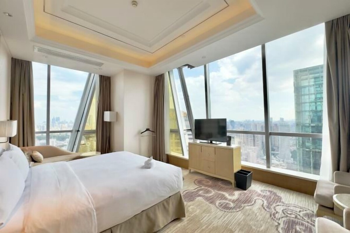 A hotel room with a large bed, a TV, a desk, and a view of the city.