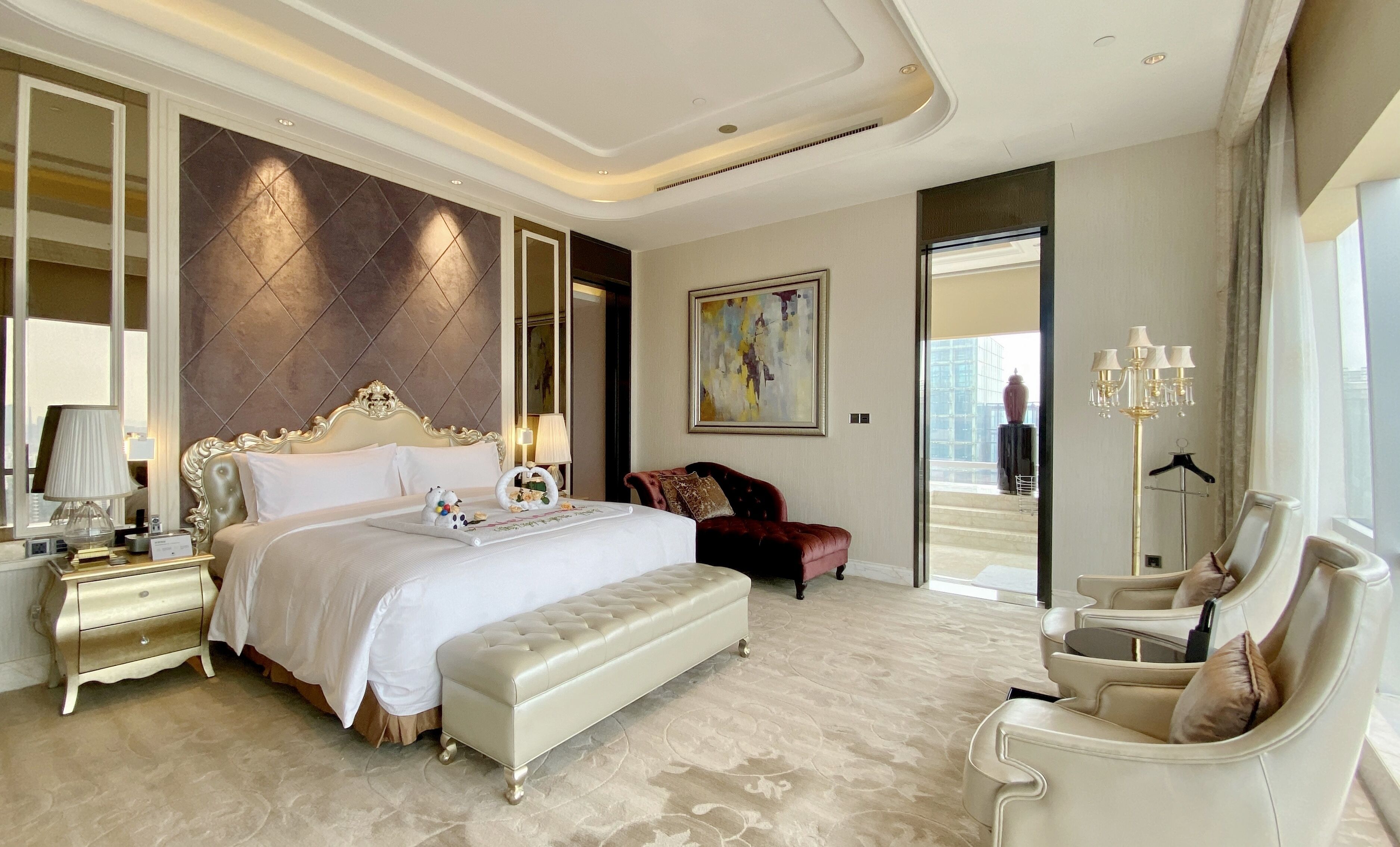 A spacious bedroom with a large bed, a chaise lounge, a desk, and a floor lamp.