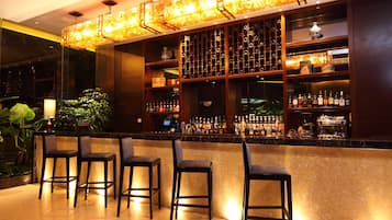 Zona de bar con estantes llenos de botellas, una máquina de café y taburetes.
