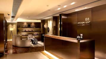 A modern reception area with a wooden reception desk, a seating area with a sofa and armchairs, and a wall-mounted shelf with decorative items.