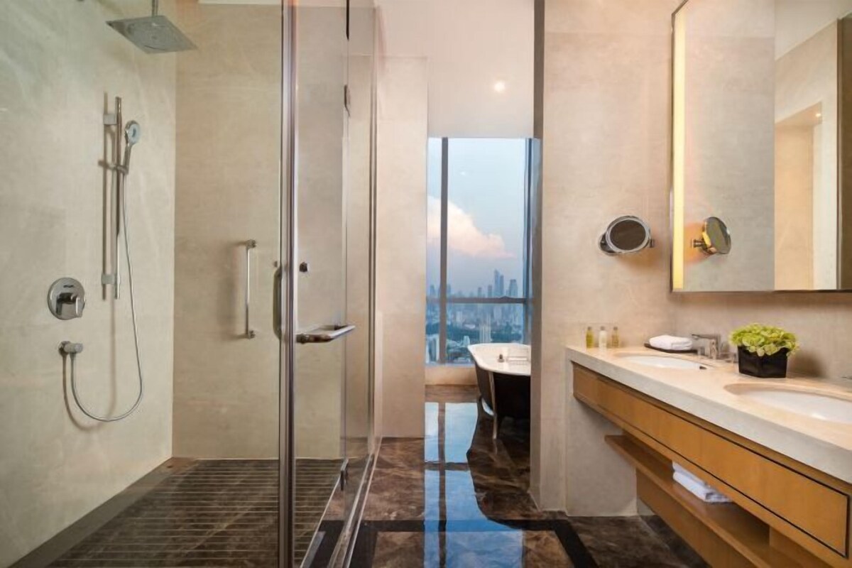 Un baño moderno con ducha envuelta en vidrio, un espejo grande y vistas a la ciudad.