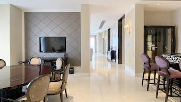 A hotel dining area with a long table and chairs, a television mounted on the wall, and a bar area with stools.