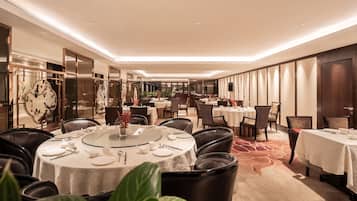 A hotel dining area with round tables, chairs, and a bar in the background.