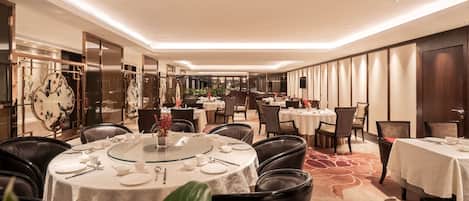 A hotel dining area with round tables, chairs, and a bar in the background.