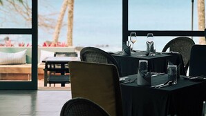 A dining area with a view of the sea, featuring tables set with glasses and cutlery, and large umbrellas providing shade. - Bom Bom – Principe Collection (Príncipe Island)