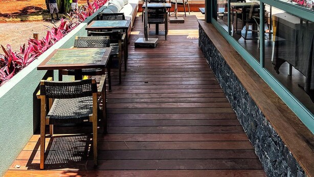 An outdoor seating area with wooden tables and chairs, surrounded by tropical plants and umbrellas, overlooking a beach. - Bom Bom – Principe Collection (Príncipe Island)