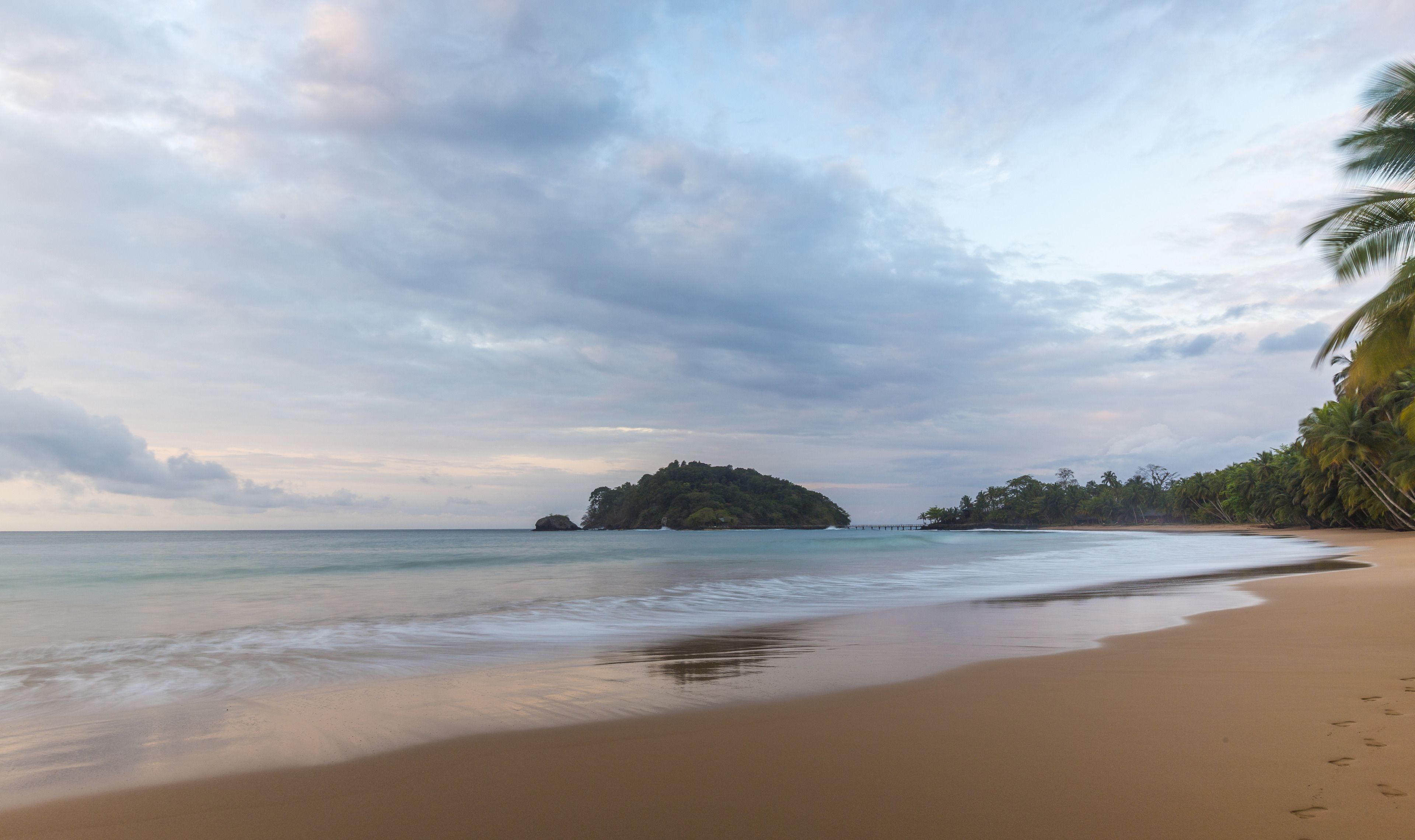 A beach with a sandy shore, calm water, and a small island in the distance.
