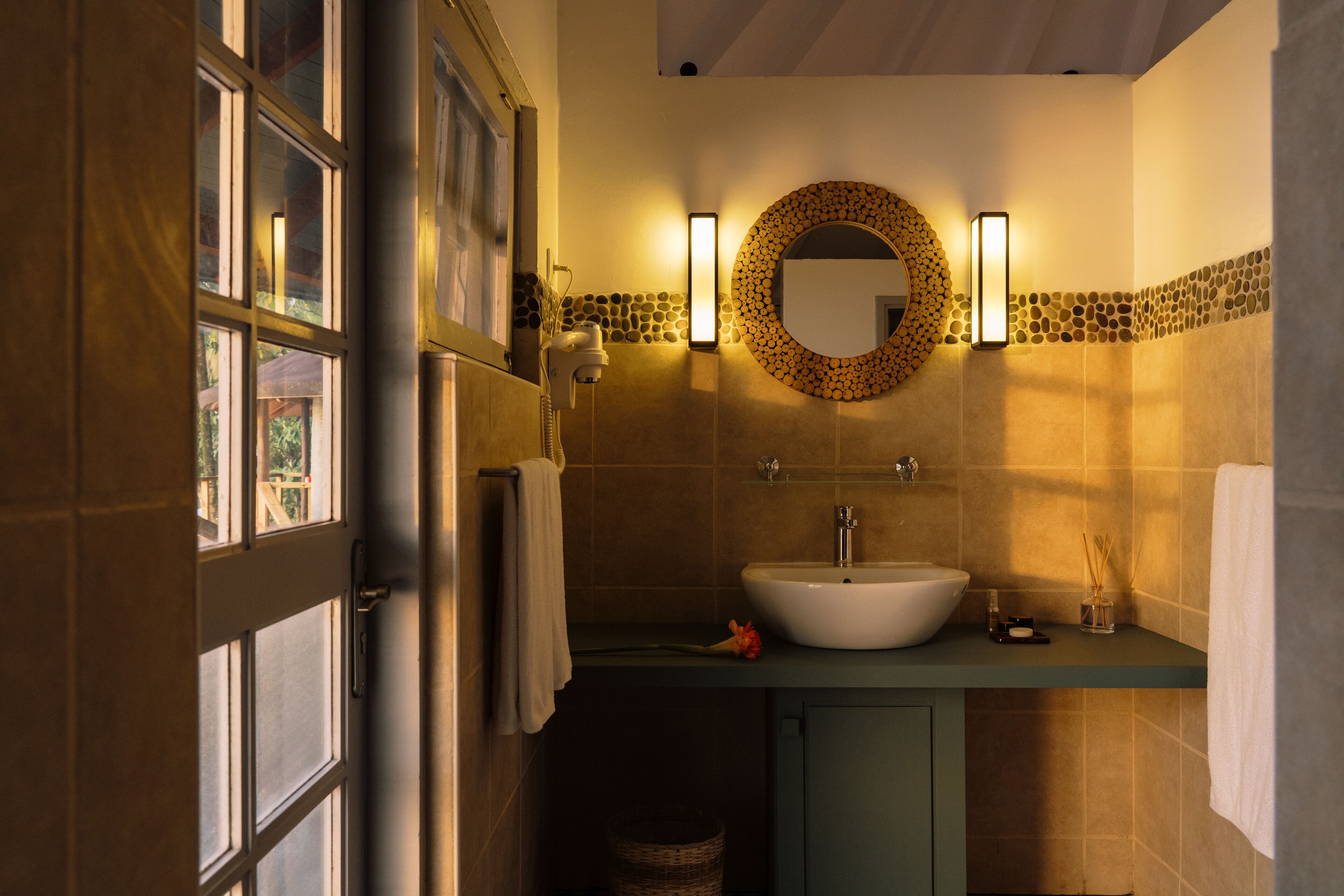 Une salle de bain avec une grande fenêtre, un lavabo, un miroir et un porte-serviettes.