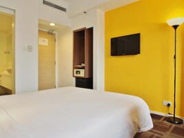 A hotel room with a large bed, a television mounted on the wall, a wardrobe, and a lamp.