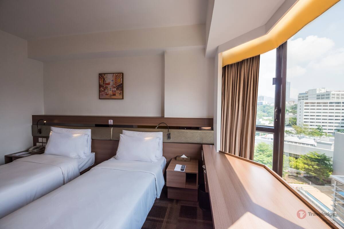A hotel room with two beds, a nightstand, a bedside table, a painting on the wall, and a window with curtains.