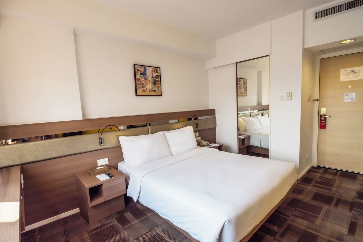 A hotel room with a bed, bedside table, lamp, and a mirror.