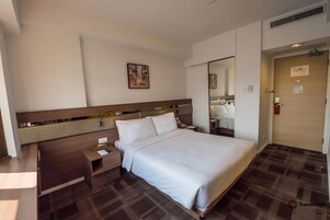 A hotel room with a large bed, a bedside table, a nightstand, a mirror, and a door with a sign.
