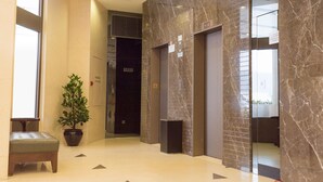 A modern lobby with marble walls, a potted plant, a bench, and an elevator. - Travelodge Kowloon (Kowloon)