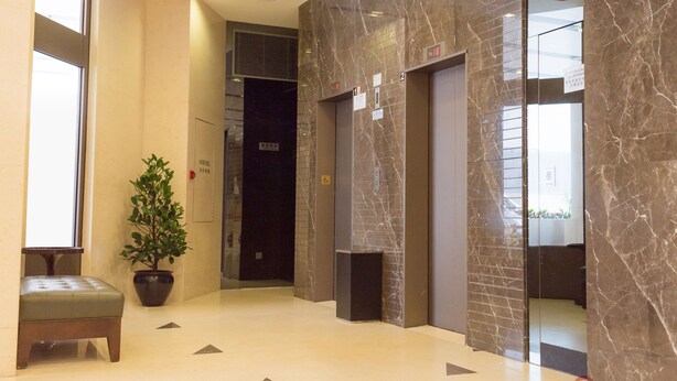 A modern lobby with marble walls, a potted plant, a bench, and an elevator.