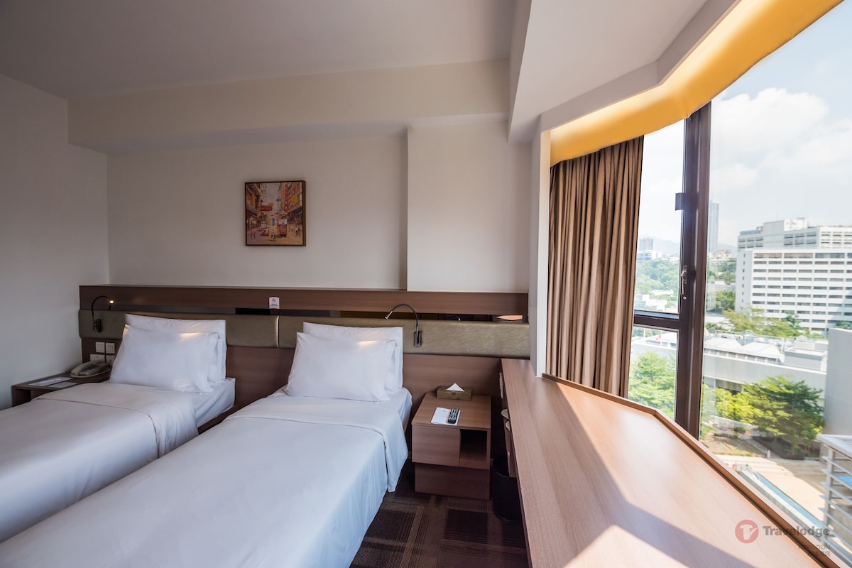 Une chambre d’hôtel avec deux lits, une table de chevet, une commode, un tableau au mur et une fenêtre avec des rideaux.