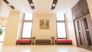 A lobby with a marble floor, a green bench, red benches, and a painting on the wall.