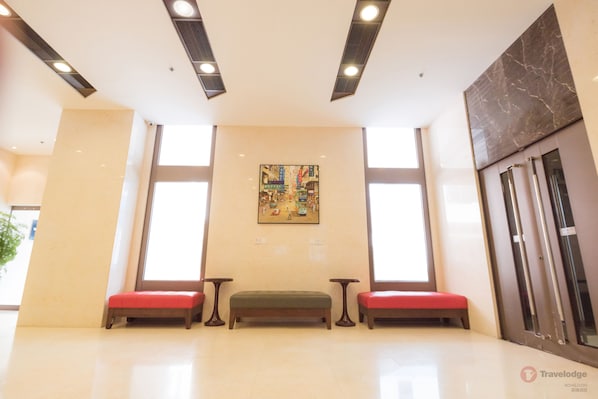 Un vestíbulo con piso de mármol, un banco verde y bancos rojos, y un cuadro en la pared.