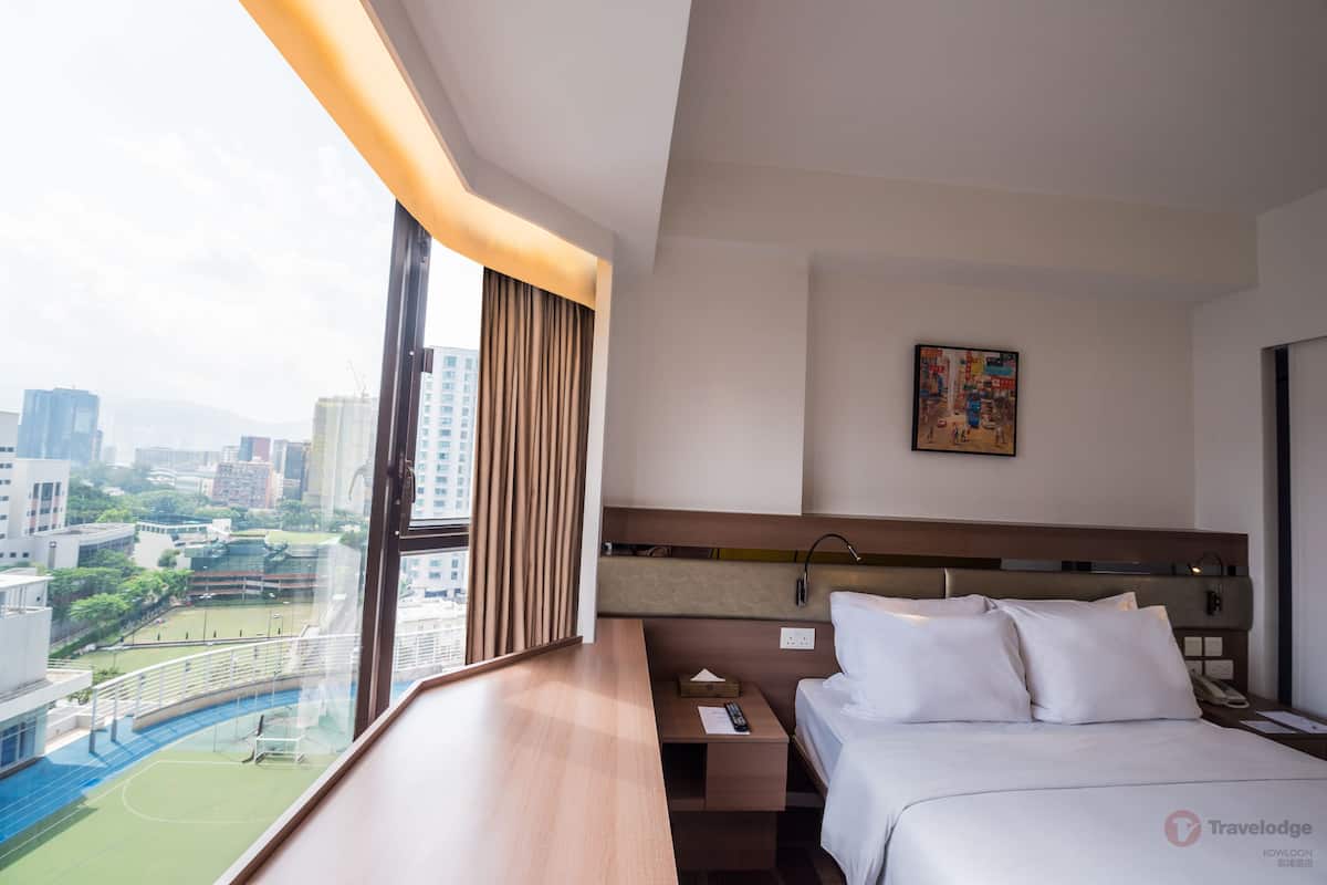 A hotel room with a large window, a bed, a bedside table, and a nightstand.