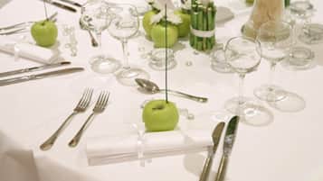 Uma mesa posta com talheres, maçãs verdes, copos de vinho e toalha de mesa branca.