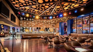 A spacious lobby with a bar area, modern seating, and a large ceiling with hanging lights.