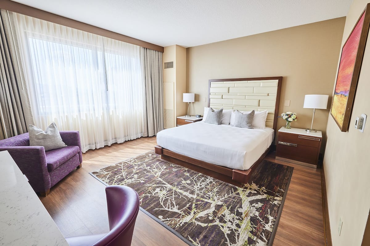 A hotel room with a large bed, a desk, a chair, and a window with curtains.