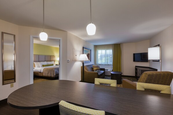 A hotel room with a large bed, a sitting area with a sofa and armchairs, a dining table, and a flat-screen TV mounted on the wall. - Candlewood Suites Tucson by IHG (Tucson)