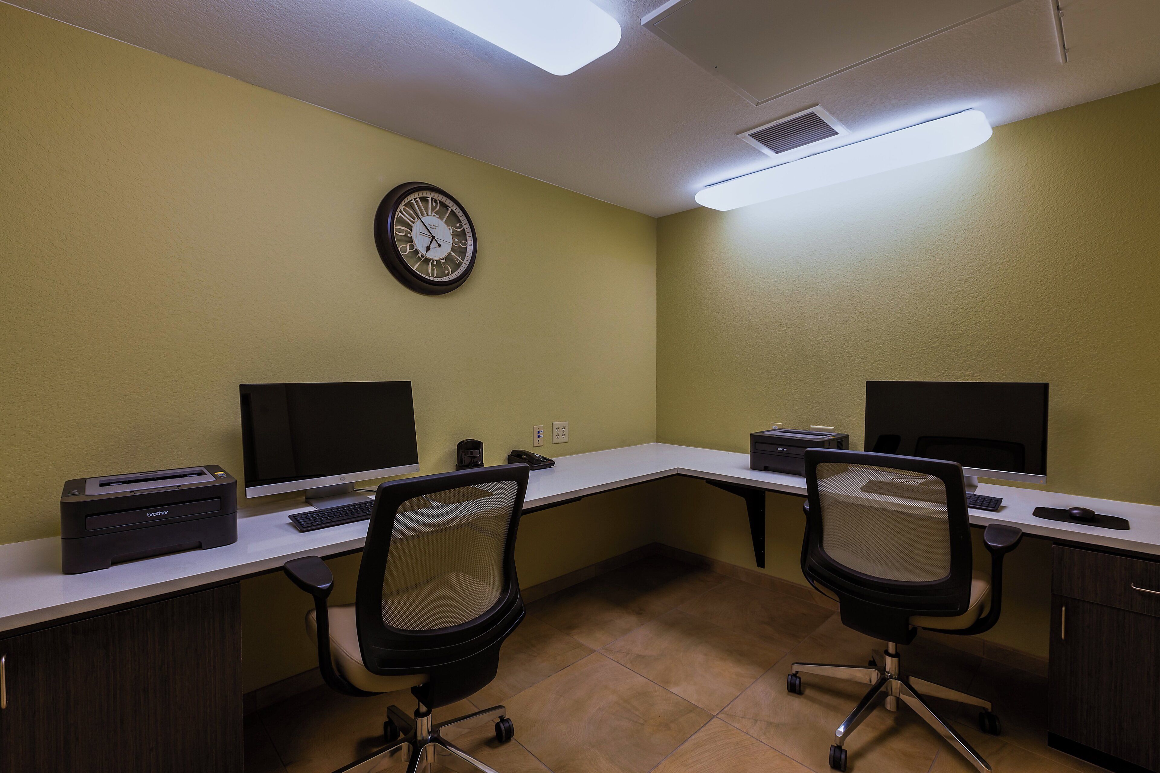 A conference room with two desks, chairs, a clock, and a printer.