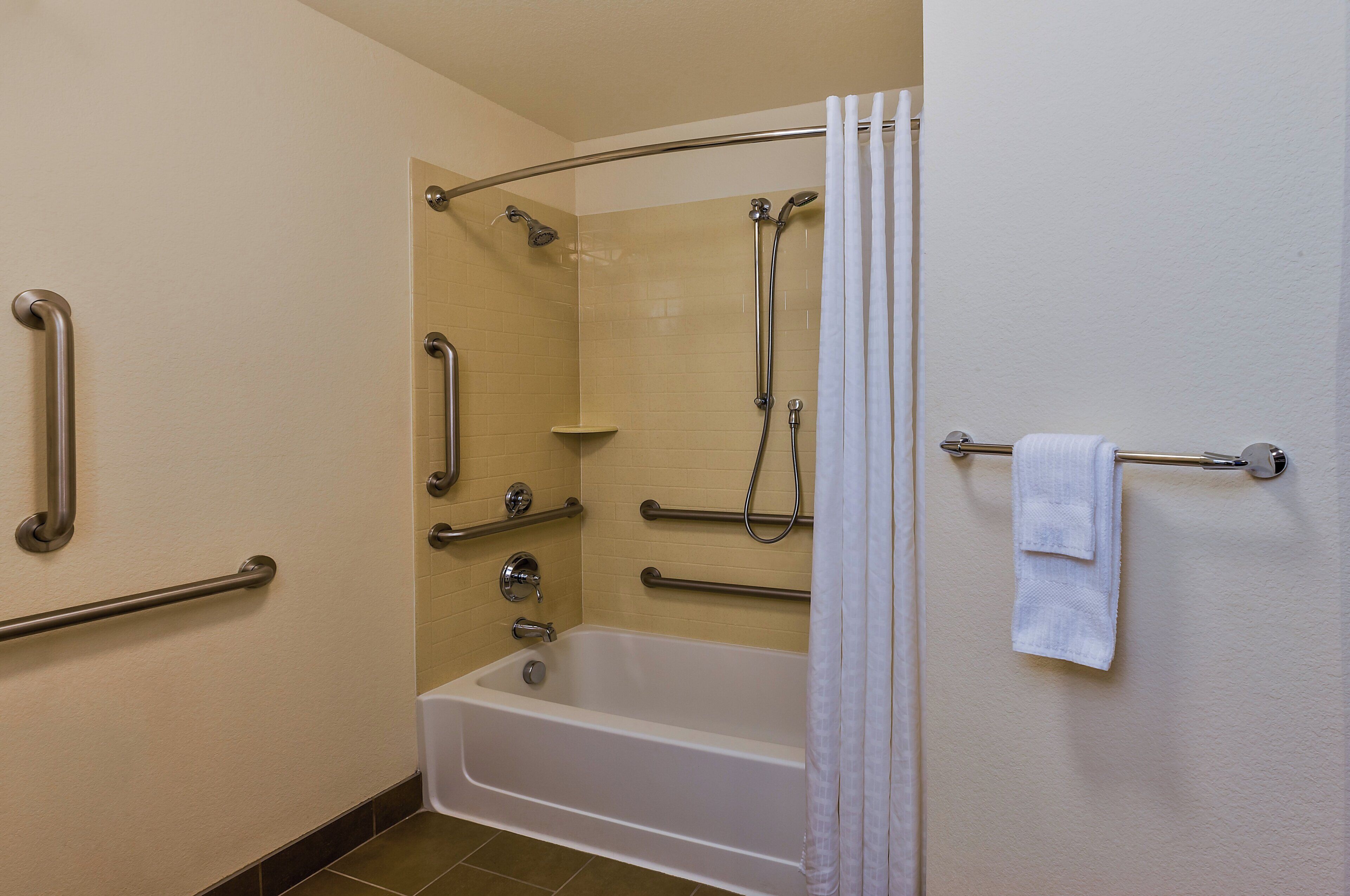 A bathroom with a bathtub, shower, grab bars, and a towel rack.