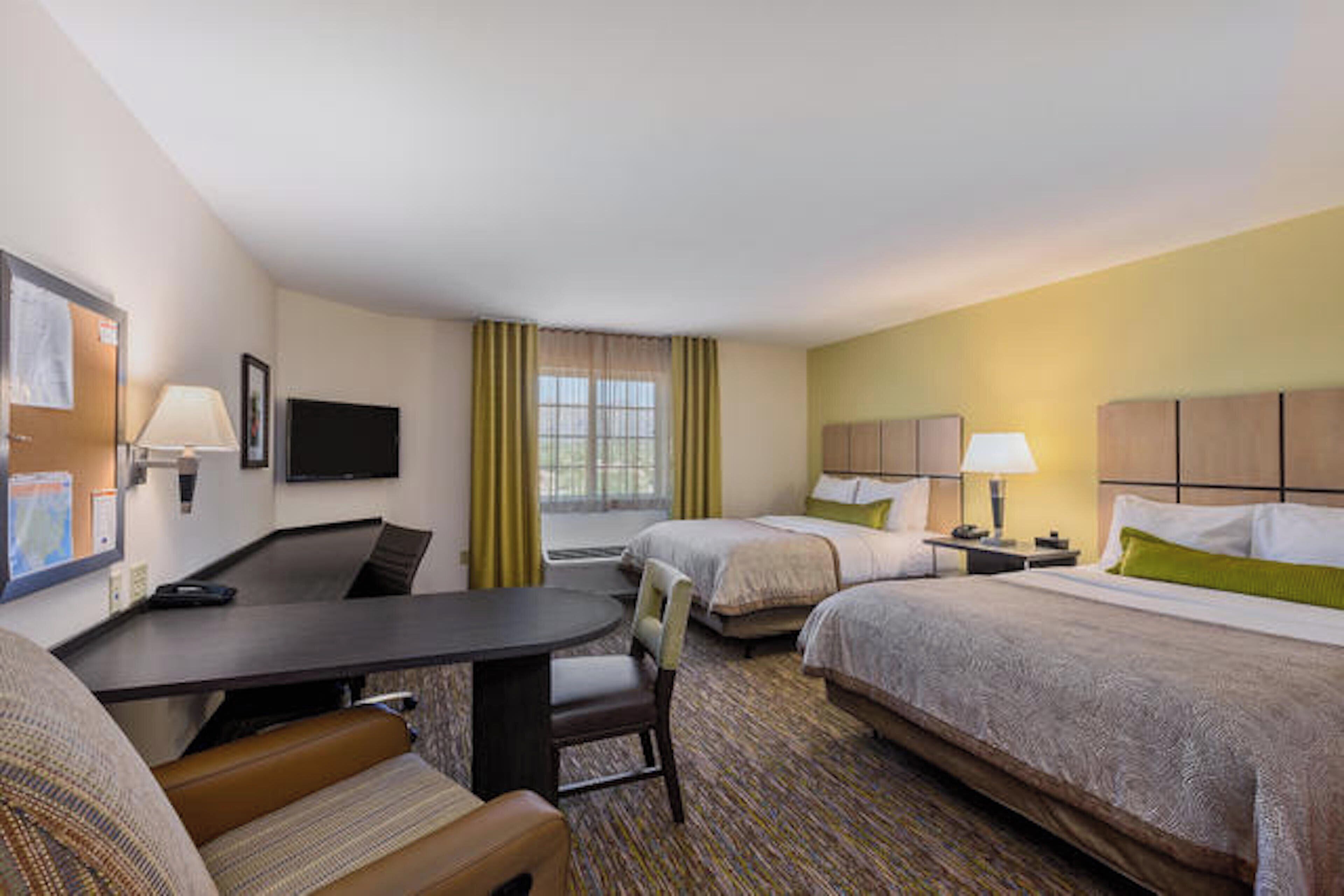 A hotel room with a desk, two beds, a chair, and a television.