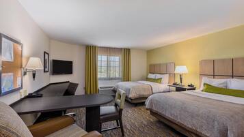 A hotel room with a desk, two beds, a chair, and a television.