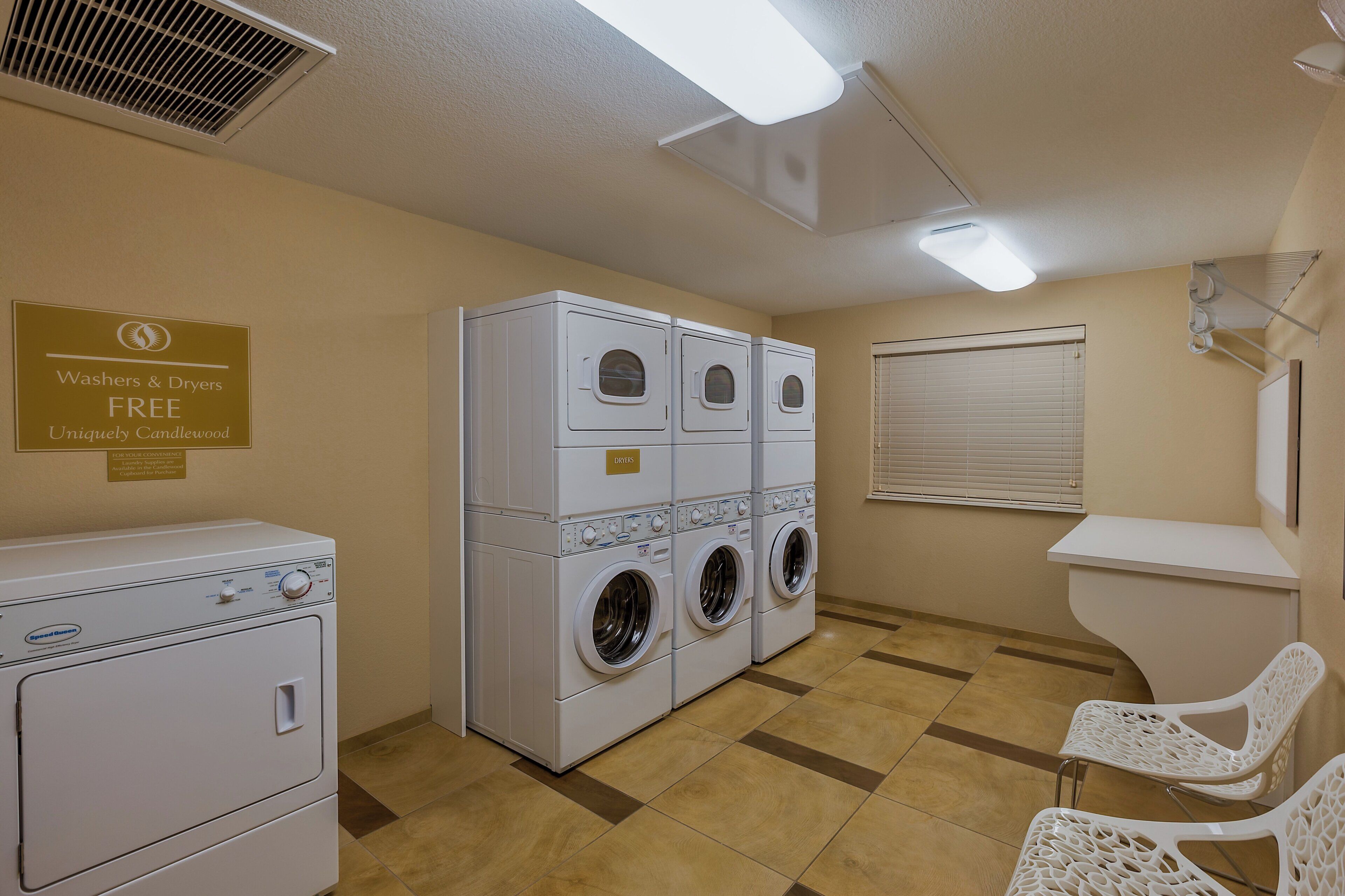 A laundry room with stacked washers and dryers, a sign offering free laundry supplies, and a window with blinds.