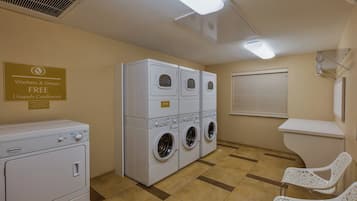 A laundry room with stacked washers and dryers, a sign offering free laundry supplies, and a window with blinds.
