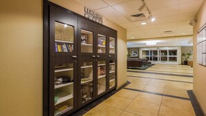 A hotel lobby with a dark wooden cabinet containing books and glasses, a tiled floor, and a reception area in the background. - Candlewood Suites Tucson by IHG (Tucson)