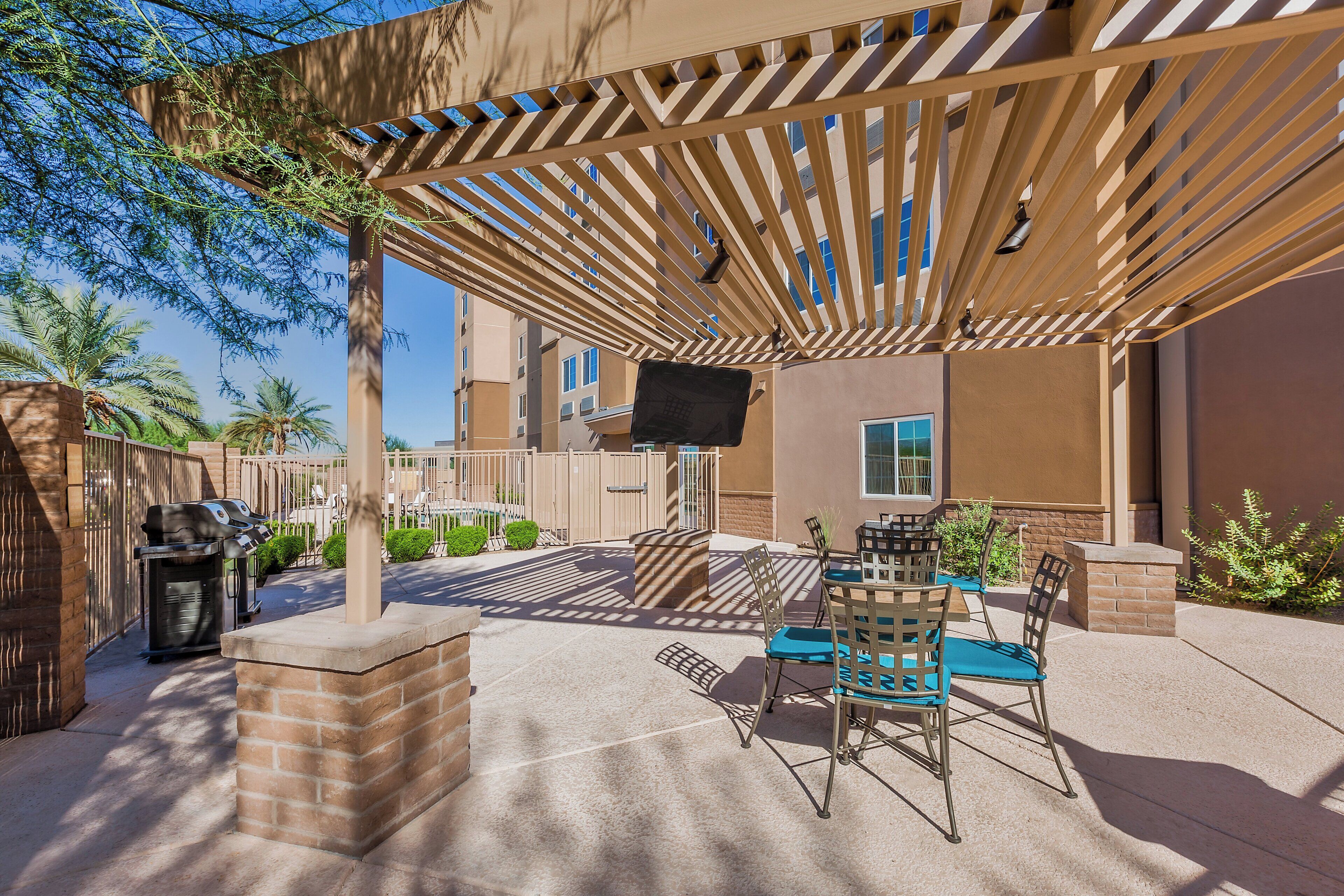 An outdoor patio with a pergola, seating area, and a barbecue grill.