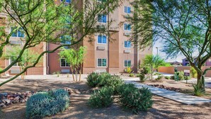 A multi-story building with a landscaped garden area featuring shrubs and trees. - Candlewood Suites Tucson by IHG (Tucson)