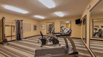 A hotel gym with exercise equipment, including a treadmill and a weight machine, carpeted flooring, and mirrors on the walls.