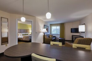 A hotel room with a bed, a seating area with a sofa and armchairs, a dining table, and a television. - Candlewood Suites Tucson by IHG (Tucson)