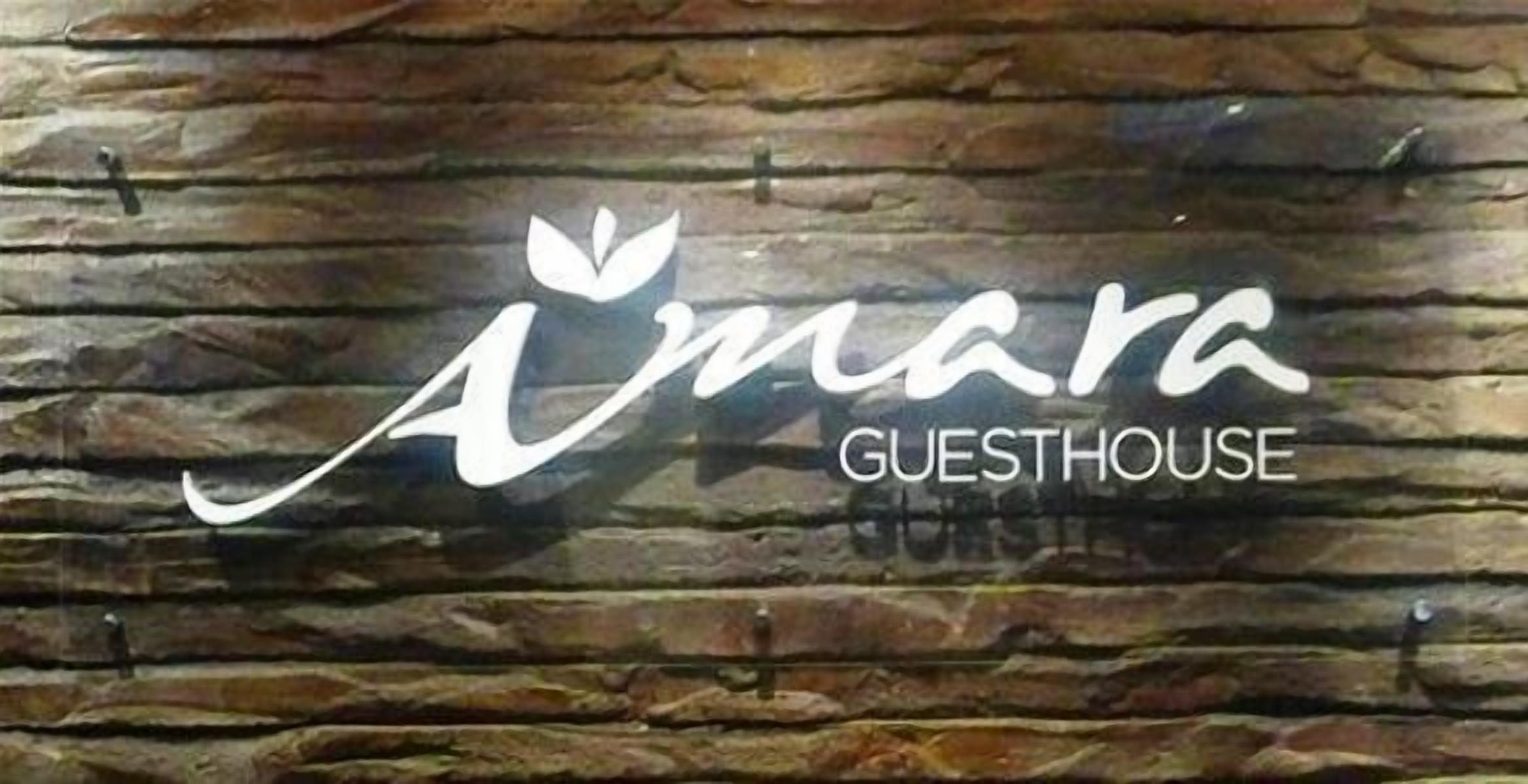 A logo with the text "Amara Guesthouse" on a wooden background.