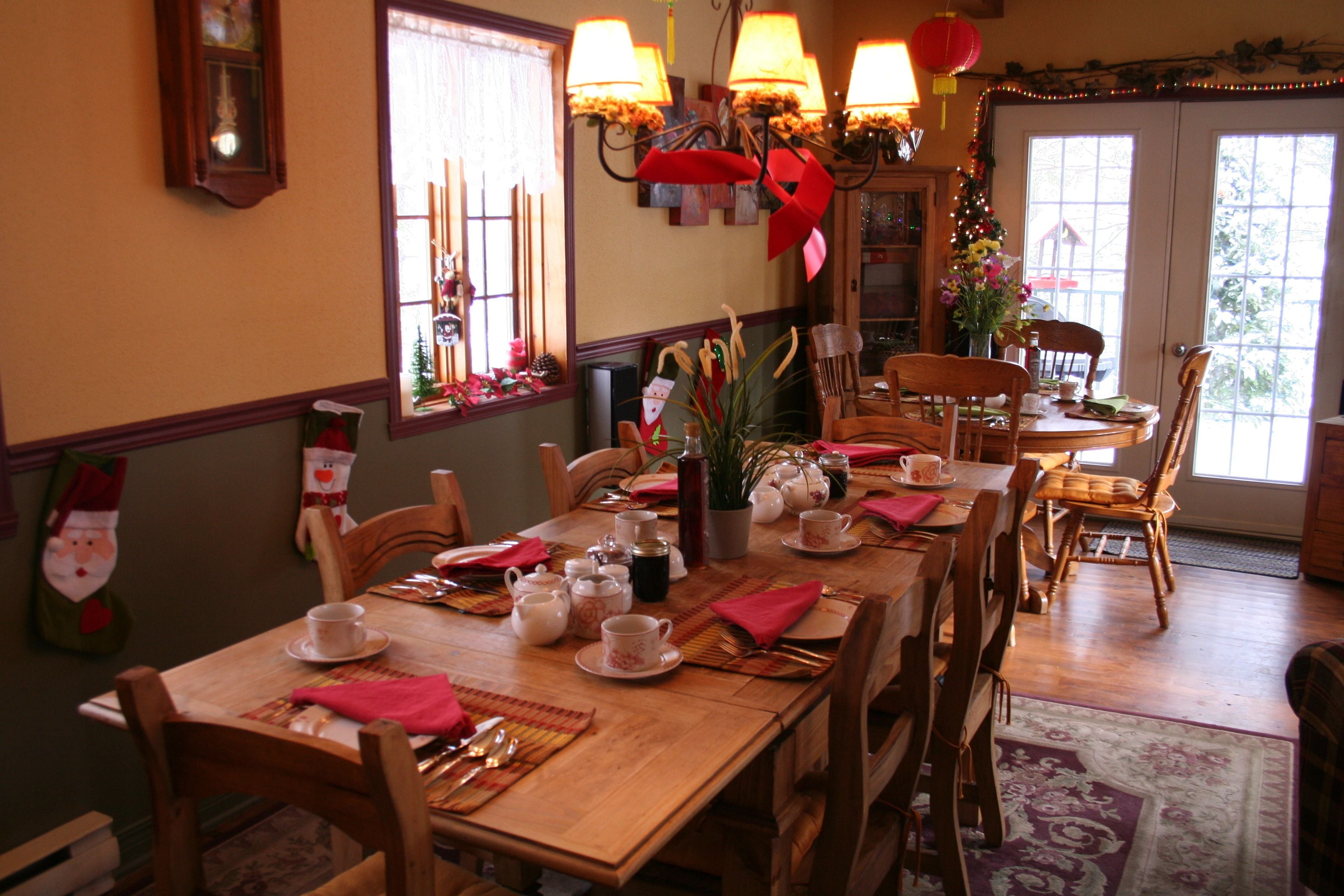 Un comedor con una mesa de madera dispuesta para cuatro, sillas y un árbol de Navidad.