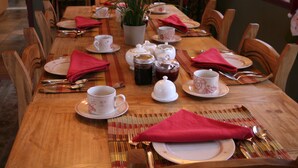 Une table à manger dressée avec des assiettes, des tasses et des couverts, entourée de chaises en bois.