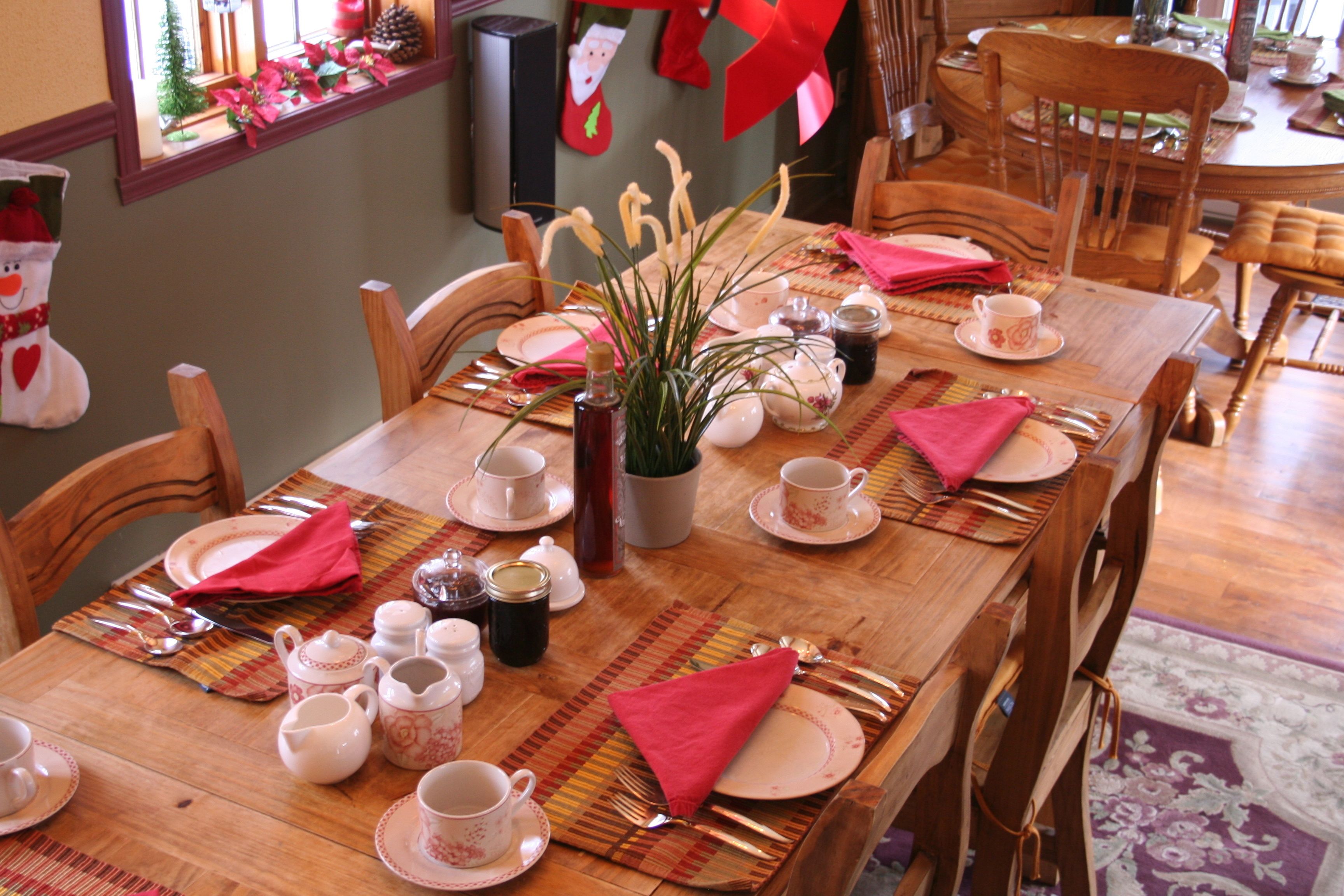 Una mesa de comedor dispuesta con platos, tazas y cubiertos, rodeada de sillas de madera.