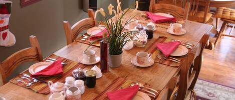 Una mesa de comedor dispuesta con platos, tazas y cubiertos, rodeada de sillas de madera.