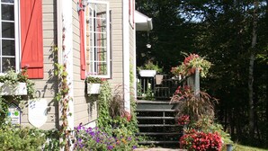 Une maison avec un chemin de pierre menant à un escalier en bois. Des plantes et des fleurs en pot bordent le chemin.