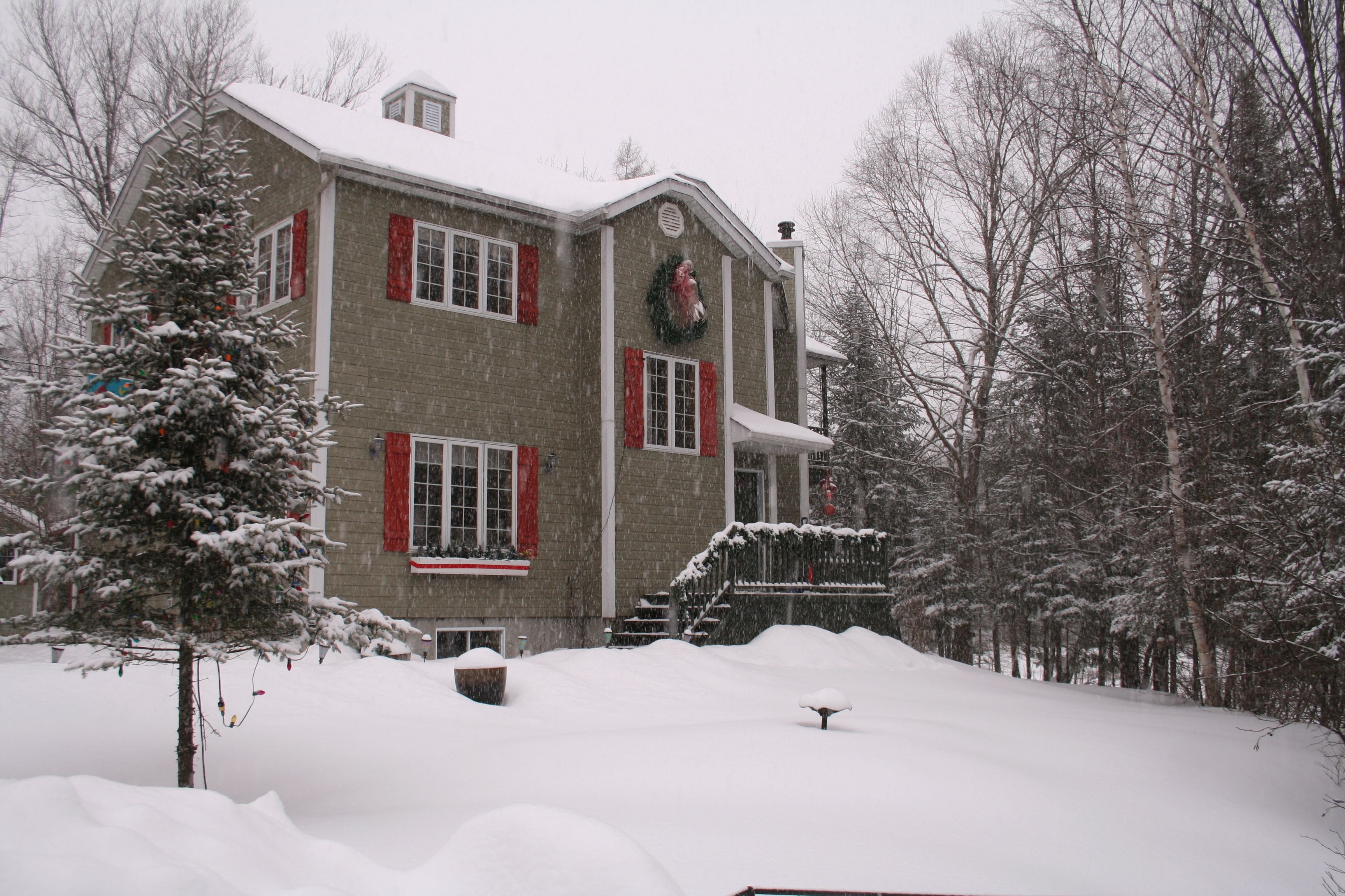 Una casa de dos pisos con fachada de ladrillo, contraventanas rojas y un césped cubierto de nieve.