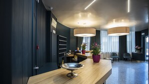 A modern reception area with a wooden reception desk, a metal bowl, potted plants, and a seating area with chairs. - Delta Hotel (Montevarchi)